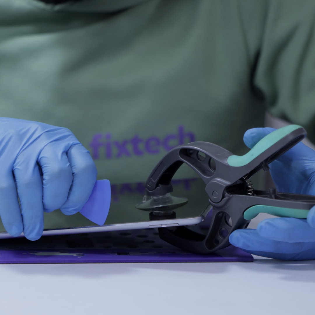 Gloved hands lifting the glass off an iPad with a suction tool and a plastic pick.