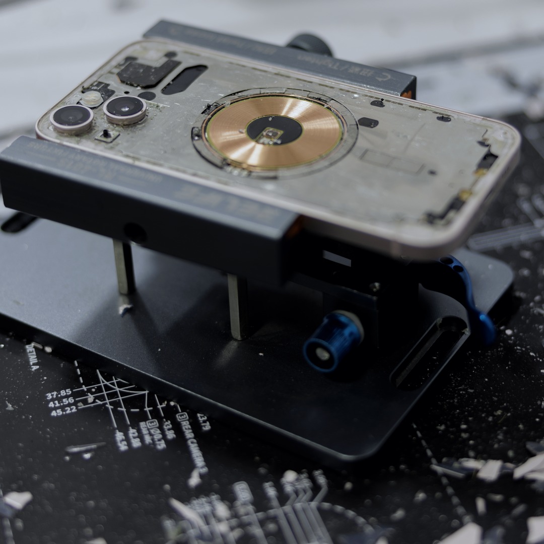 An iPhone on a repair holder with its back glass removed, showing the bare frame and the charging coil.