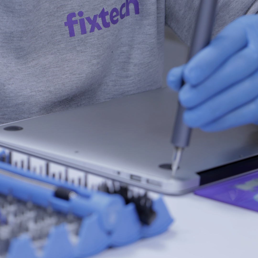 A technician in a Fixtech hoodie driving a screw into a MacBook bottom case.